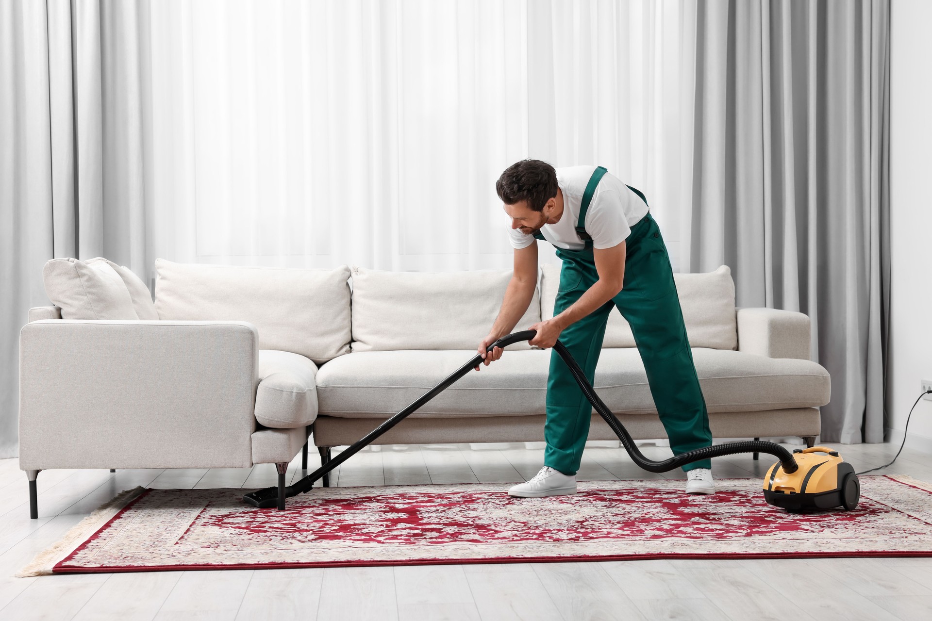Mitarbeiter der chemischen Reinigung saugen Teppich mit Staubsauger im Zimmer